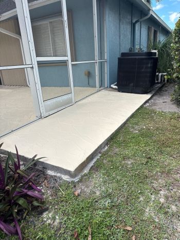 Freshly poured concrete foundation slab beside a house with screened porch and HVAC unit