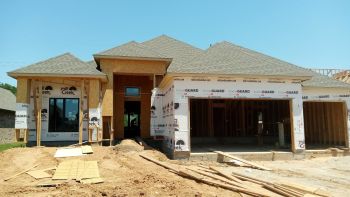 New home under construction with unfinished front entry, garage, and dirt driveway in a residential area